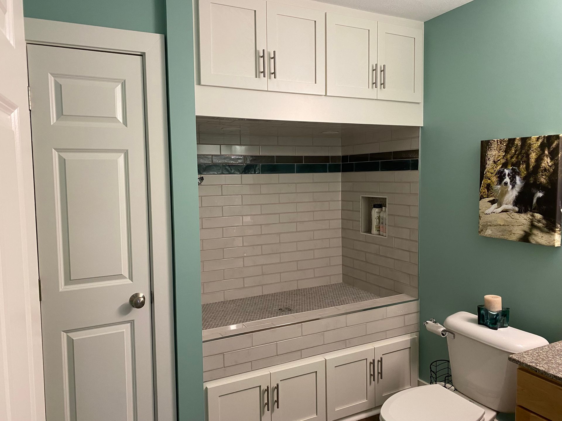 A bathroom with a tub , toilet , cabinets and a picture on the wall.