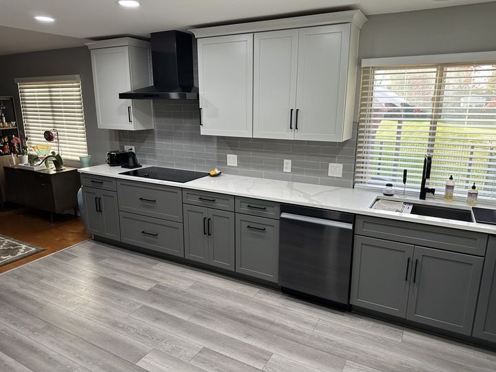 A kitchen with gray cabinets , white counter tops , stainless steel appliances and a sink.