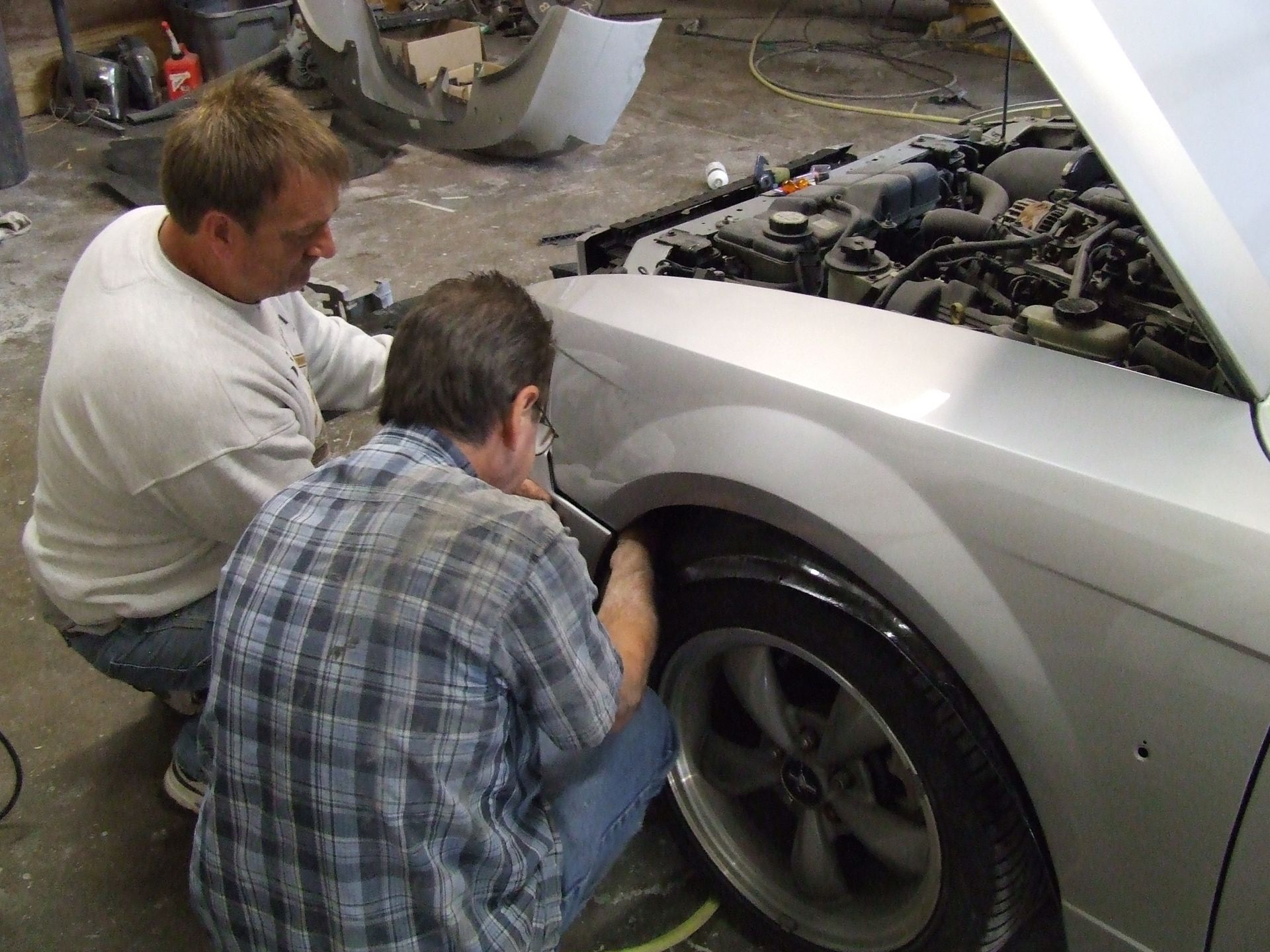 two men are working on a silver car with the hood open