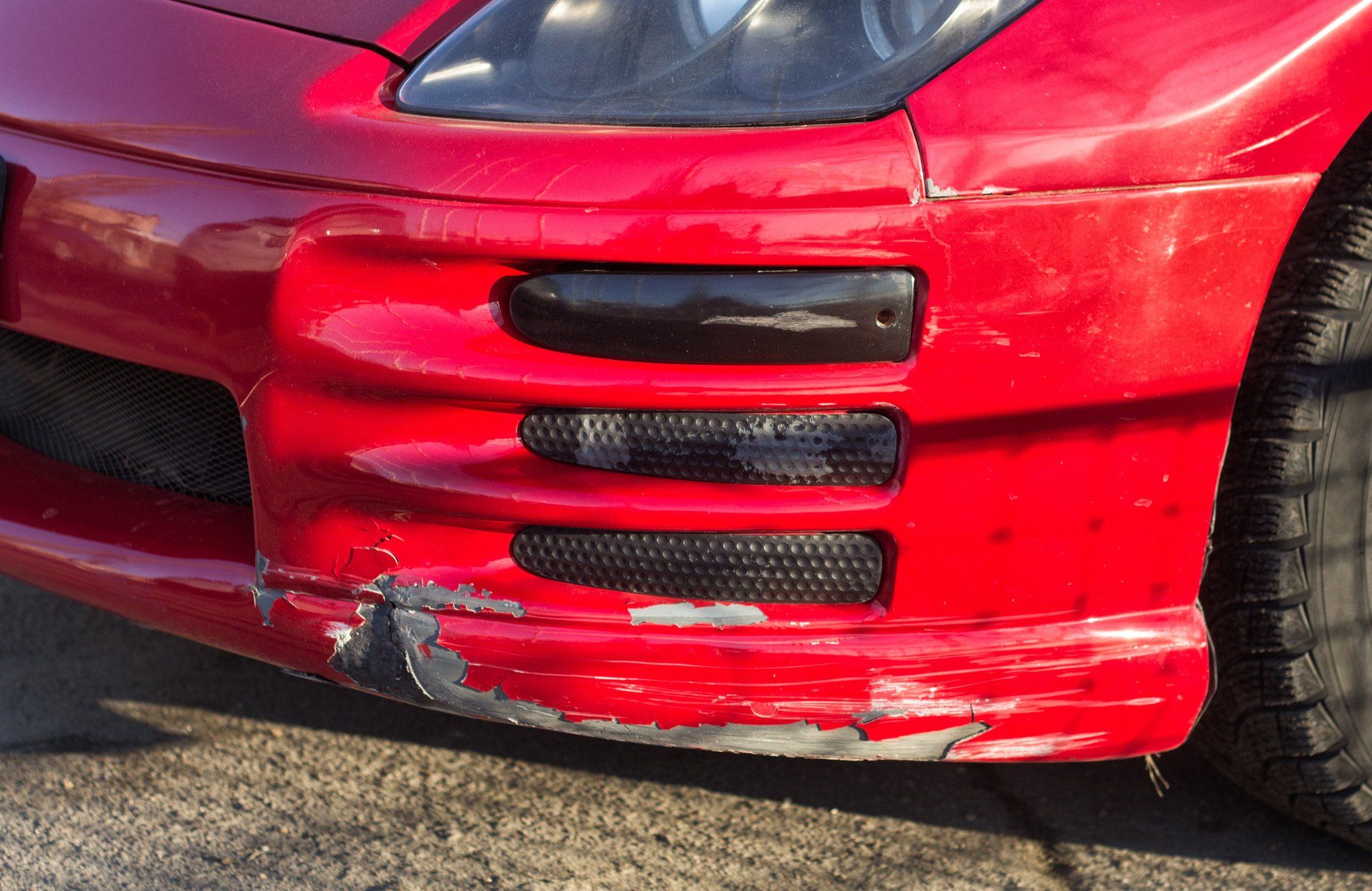 a red car with a damaged bumper is parked on the side of the road .