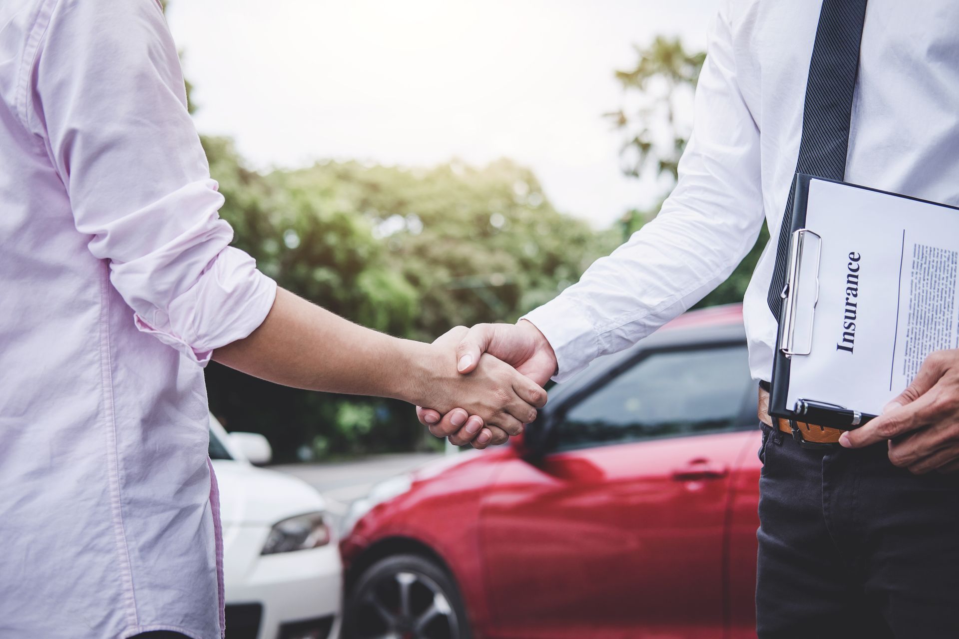 a man and a woman are shaking hands in front of a red car .