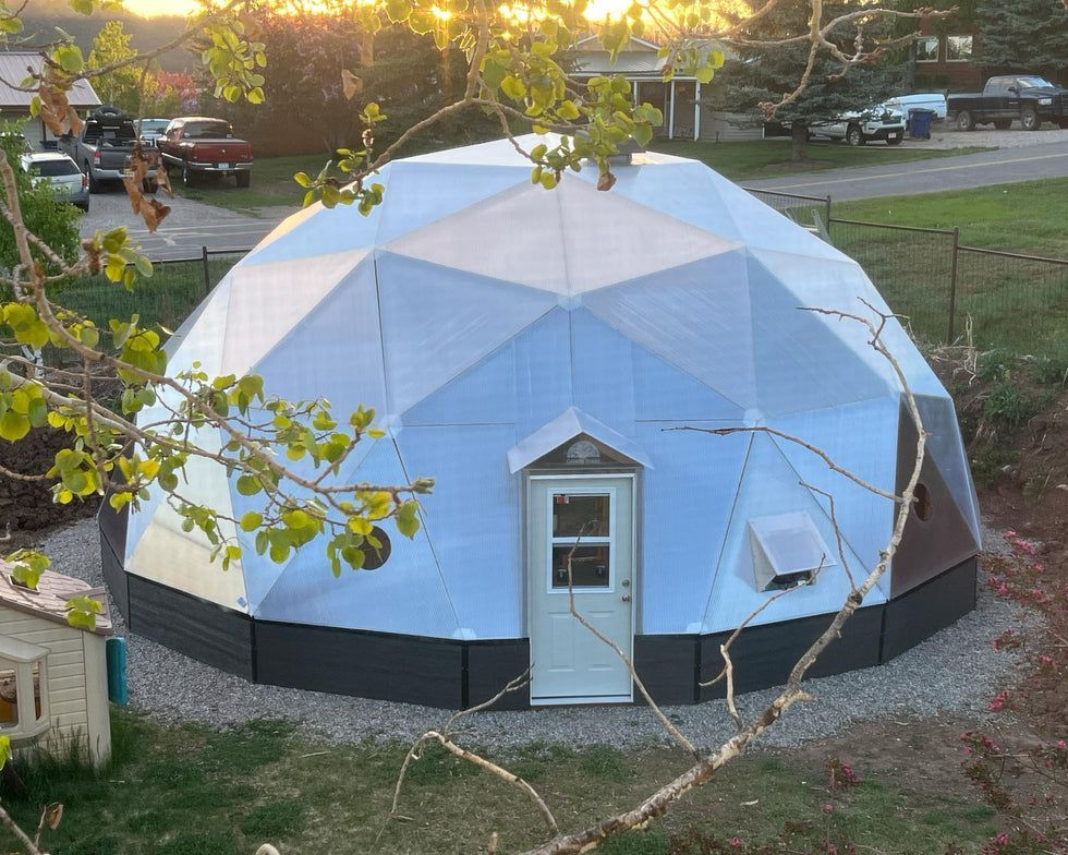 A single-story house with a grey garage door, white walls, and a green lawn under a blue sky.