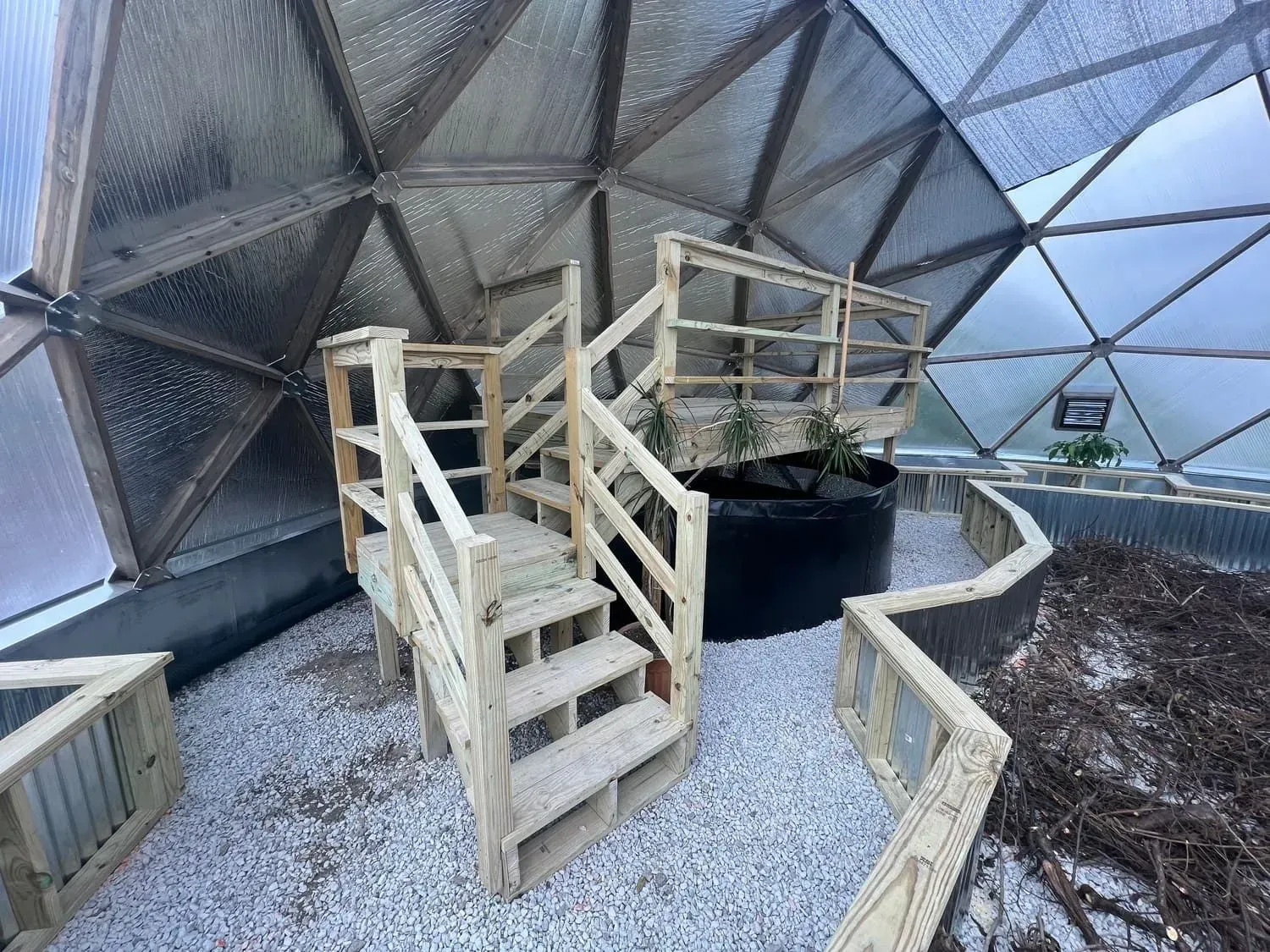 Interior view of a geodesic dome greenhouse with wooden stairs and a raised garden bed.