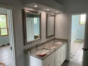 Bathroom with dual sinks, mirrors, and granite countertop; white cabinetry; light blue walls.