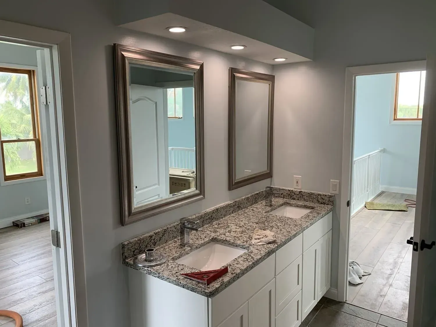 Bathroom with dual sinks, mirrors, and granite countertop; white cabinetry; light blue walls.