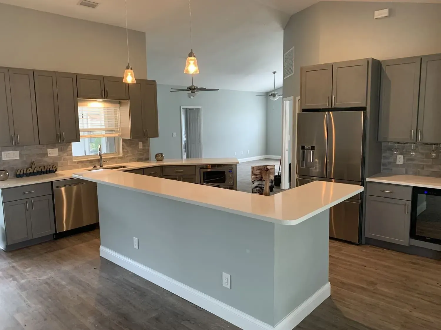 Modern kitchen with gray cabinets, white countertops, stainless steel appliances, and a breakfast bar.
