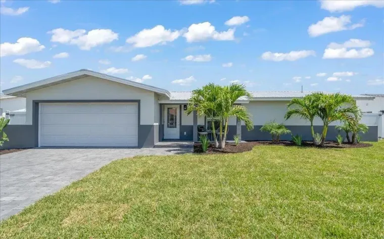 A single-story house with a grey garage door, white walls, and a green lawn under a blue sky.