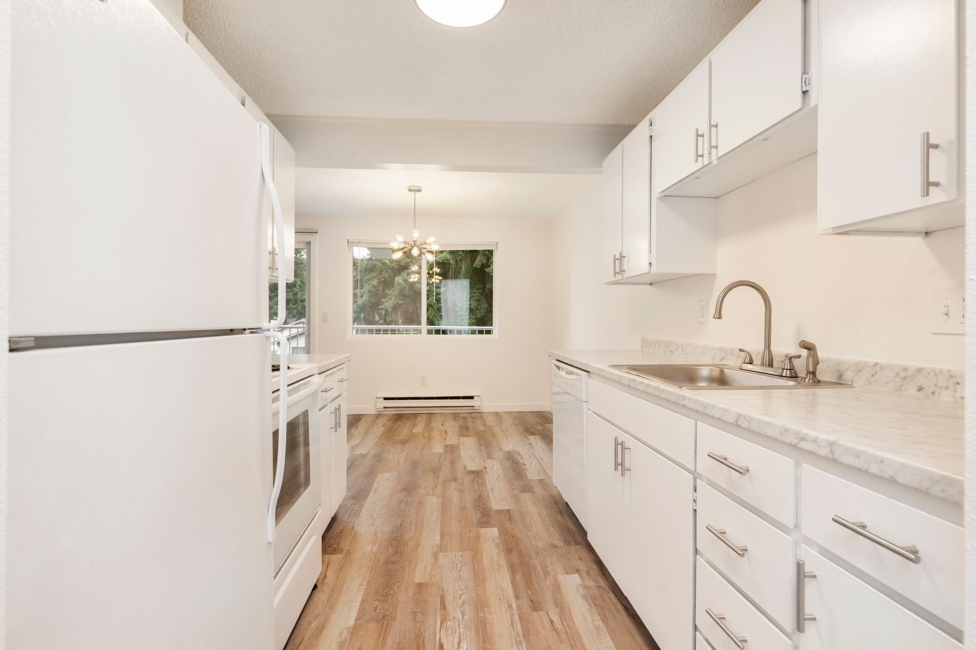 a kitchen with white cabinets , a refrigerator , a sink , and a wooden floor .
