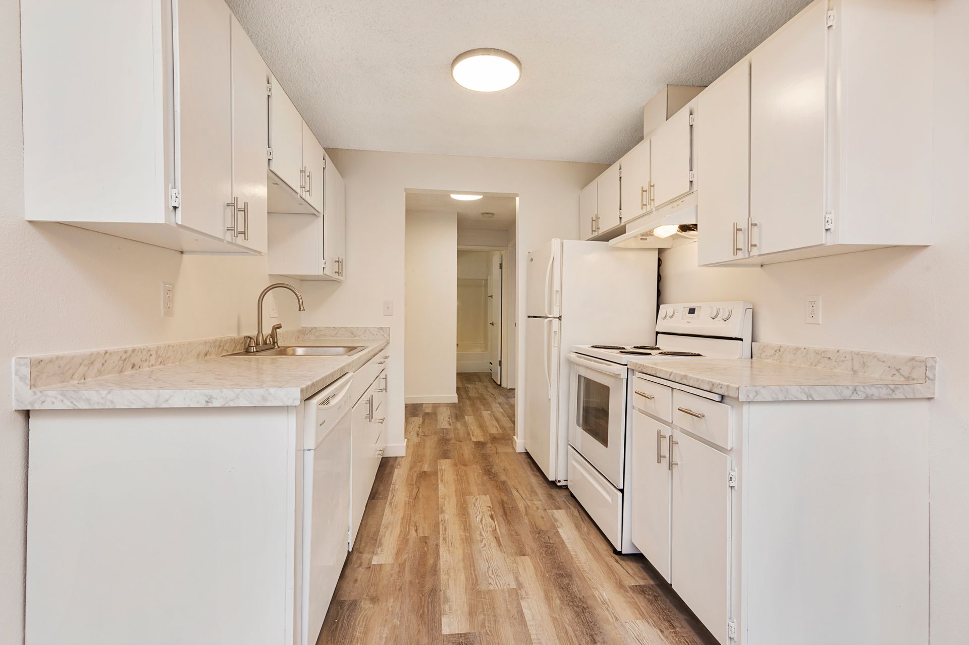 a kitchen with white cabinets , a stove , a refrigerator , and a sink .
