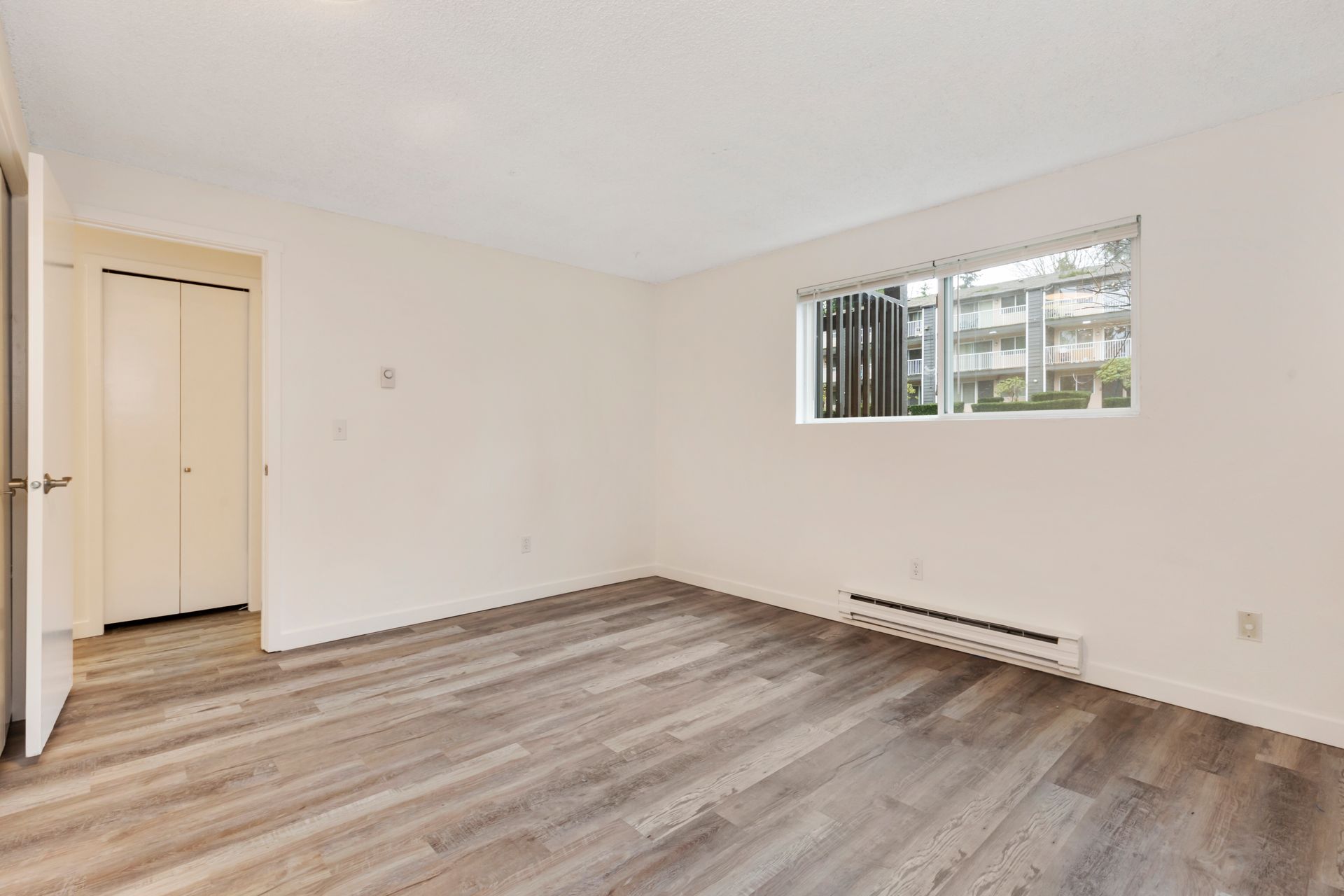 an empty living room with hardwood floors and a window .