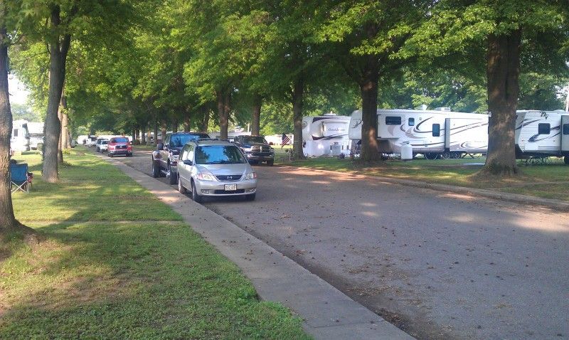 A white recreational vehicle driving along a paved road next to a calm lake and rolling.