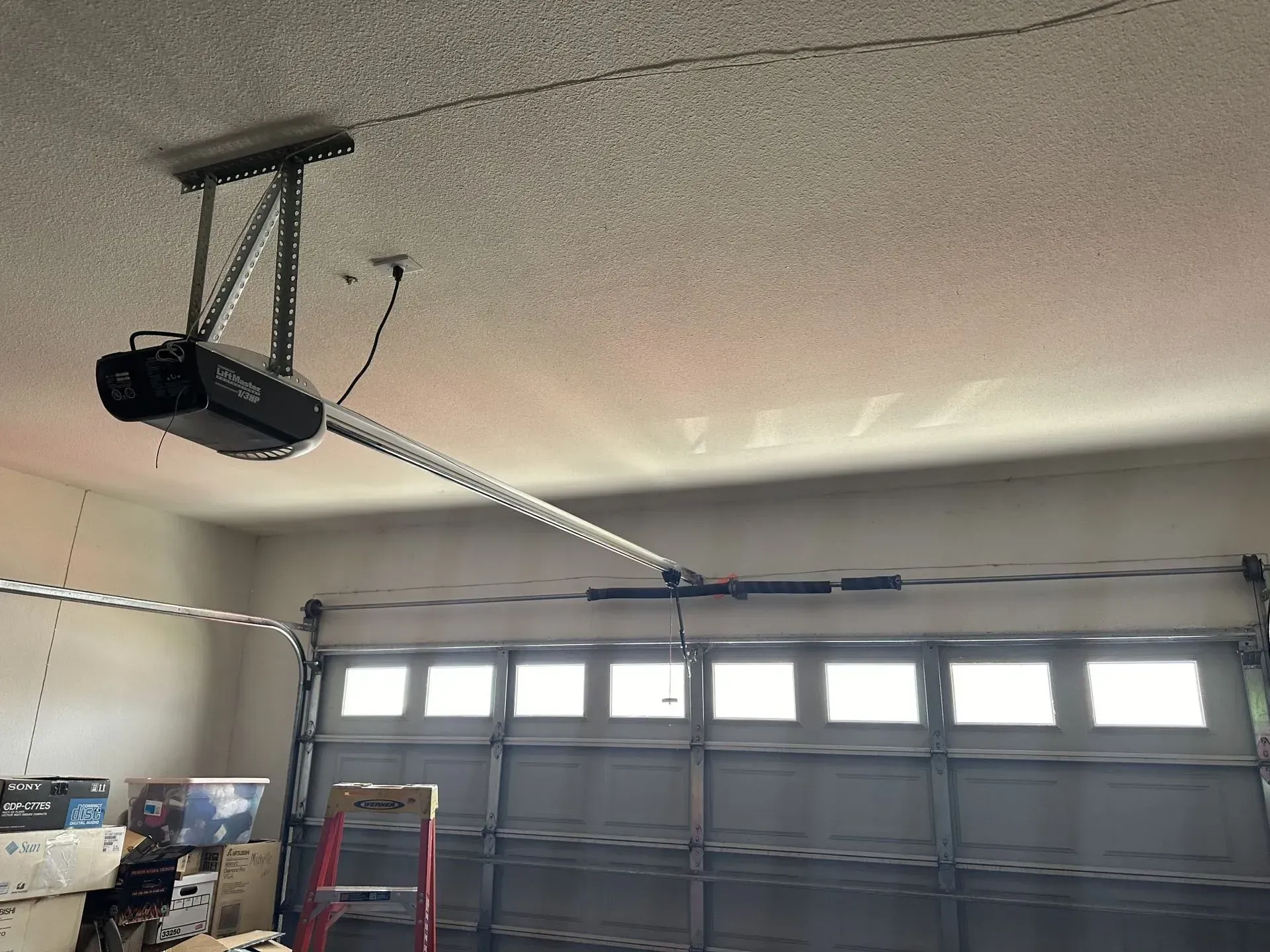 A garage door opener is hanging from the ceiling above a garage door.