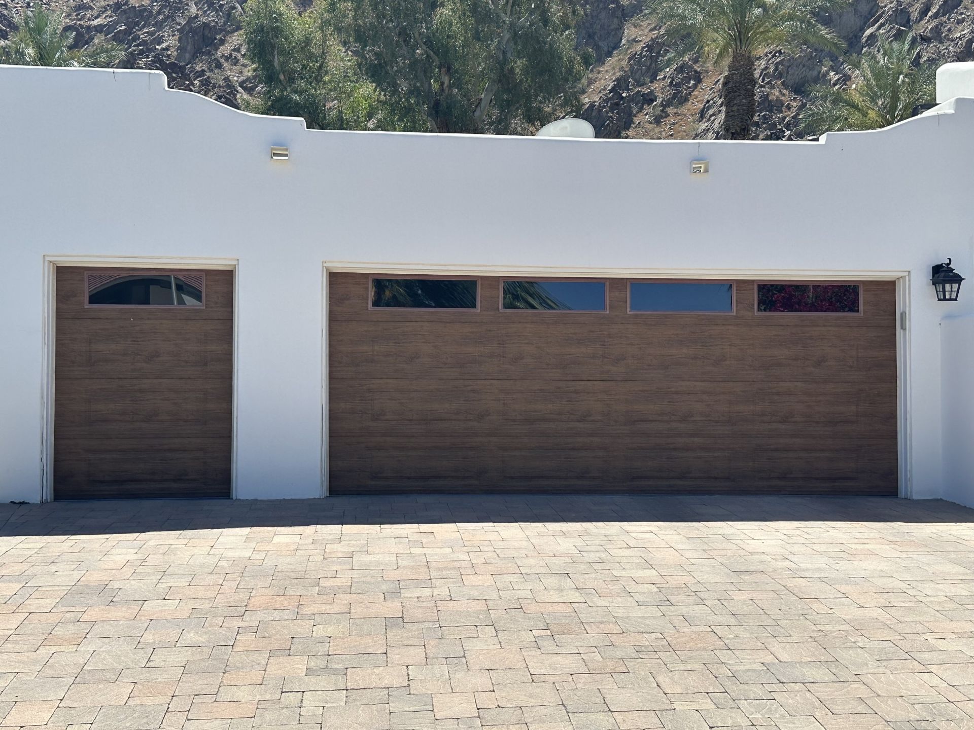 A white building with two brown garage doors and a brick driveway