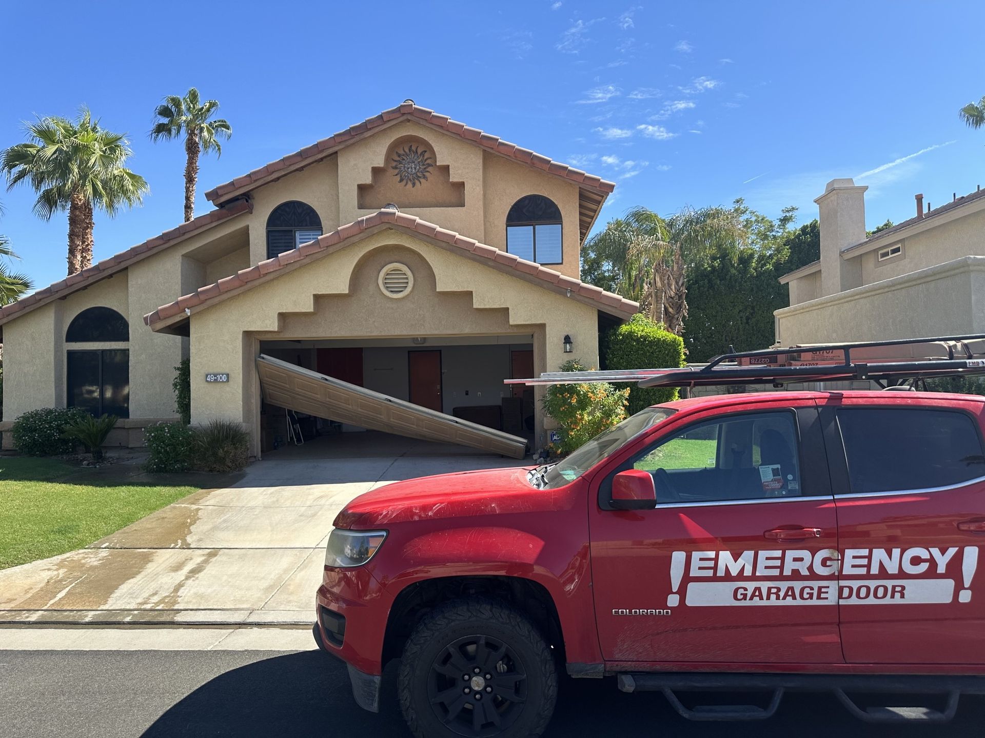 A red emergency garage door truck is parked in front of a house with a broken garage door.