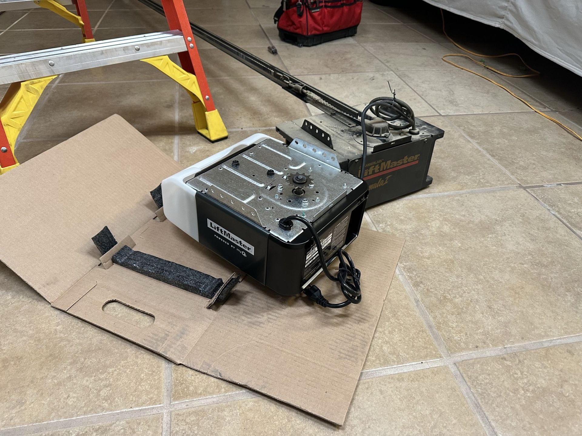 A garage door opener is sitting on the floor next to a ladder.