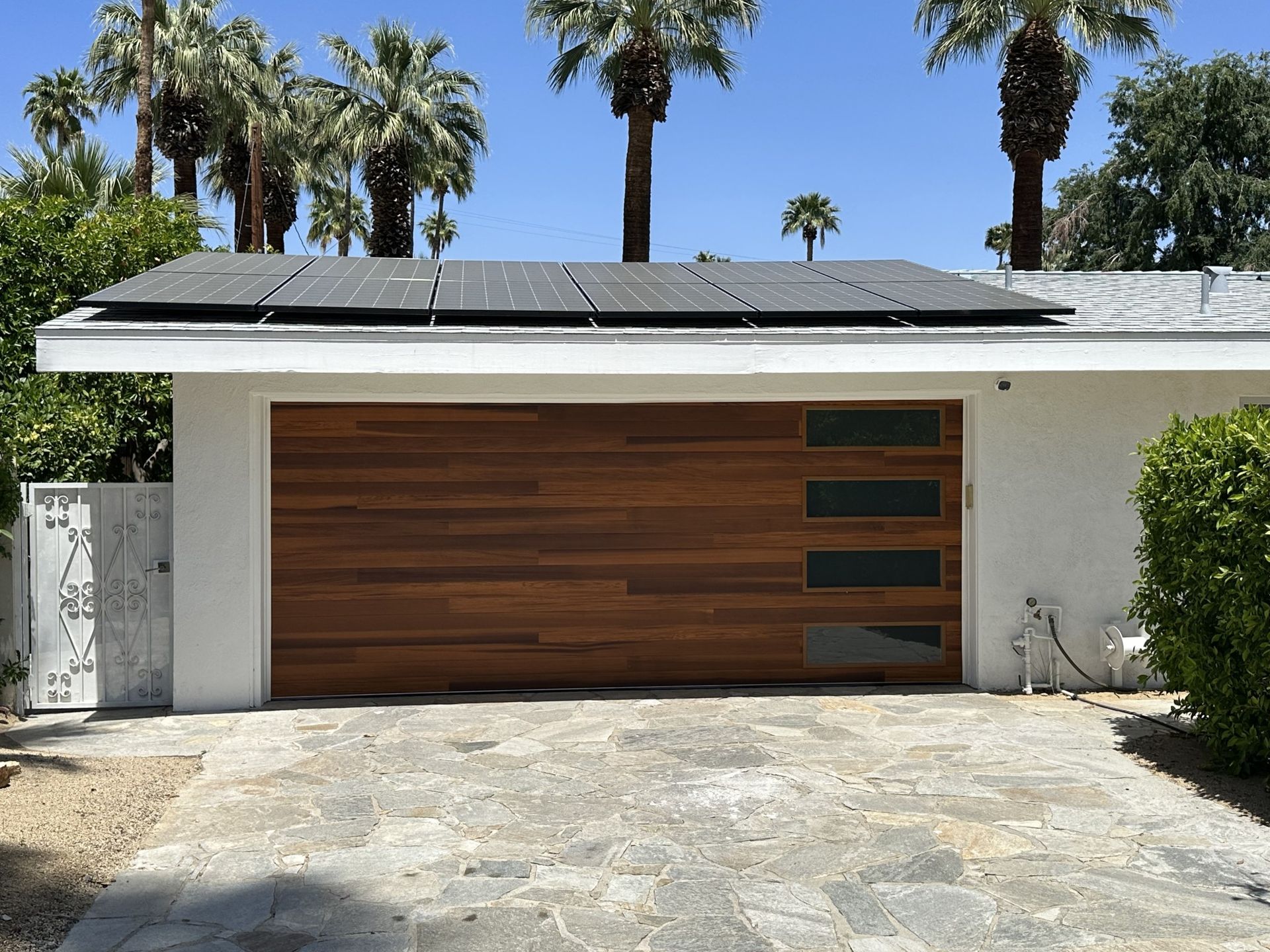 A white house with a wooden garage door and solar panels on the roof
