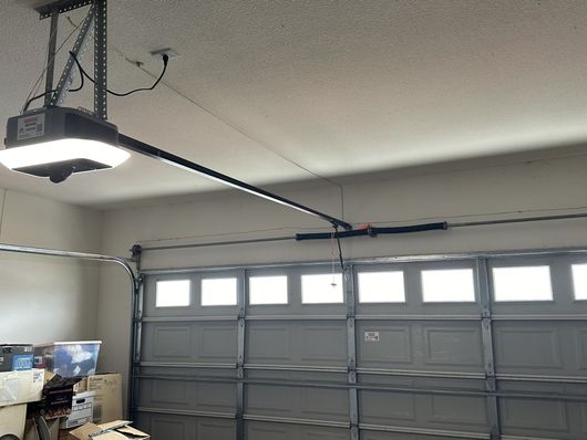 A garage door opener is hanging from the ceiling above a garage door.