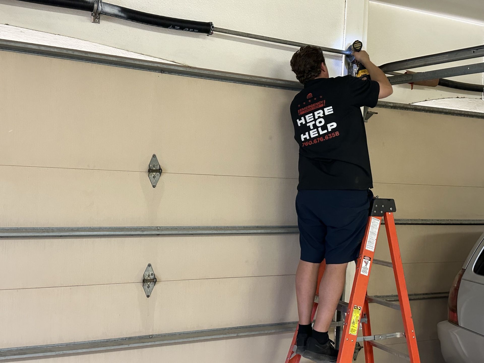 A man is standing on a ladder fixing a garage door.