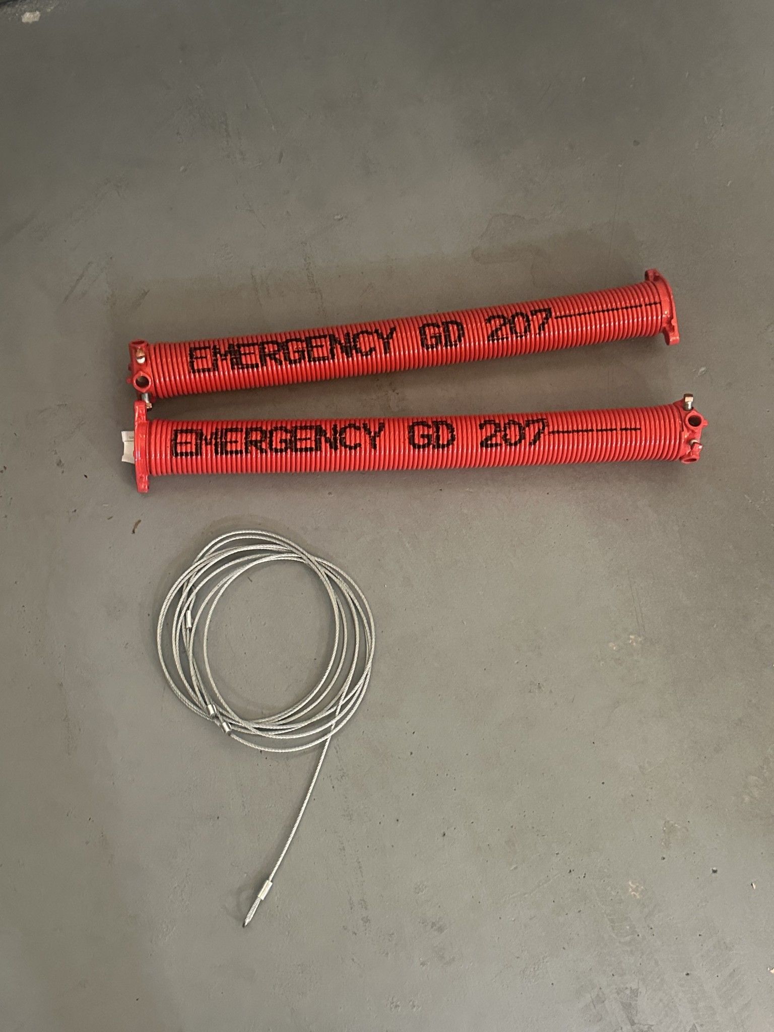 A pair of red jump ropes and a cord are sitting on a concrete surface.