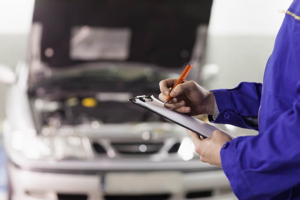 A Mechanic is Writing on a Clipboard in Front of a Car — Auto Maniac in Mossman, QLD
