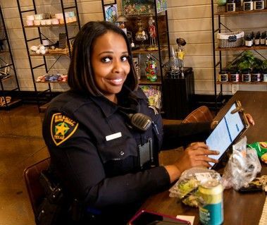A woman in a police uniform is sitting at a table using a tablet.