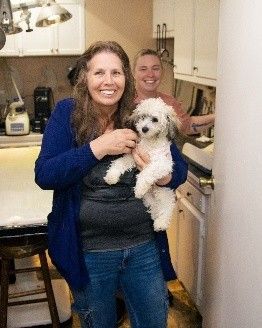 A woman is holding a small white dog in her arms in a kitchen.