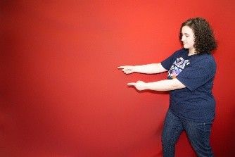 A woman in a blue shirt is standing in front of a red wall.
