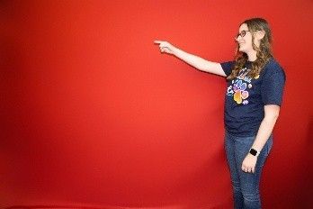 A woman is pointing at something in front of a red wall.