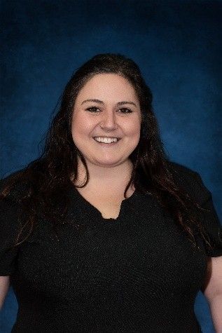 A woman in a black shirt is smiling in front of a blue background.