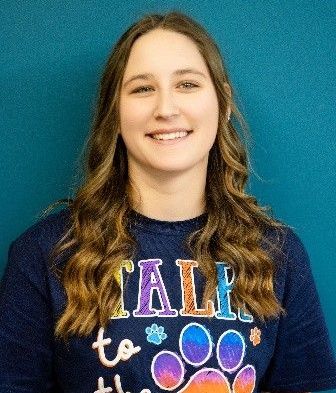 A woman wearing a blue t-shirt that says `` talk to the dog '' is smiling.