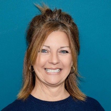 A woman in a blue shirt is smiling for the camera.