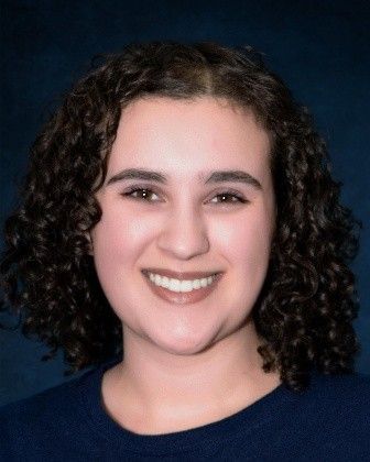 A woman with curly hair is smiling and wearing a blue shirt.