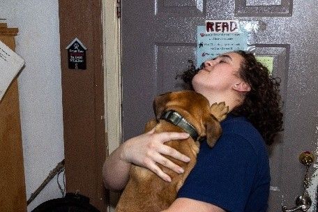 A woman is hugging a brown dog in front of a door with a read sign on it