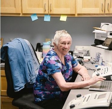 An older woman is sitting at a desk with a phone