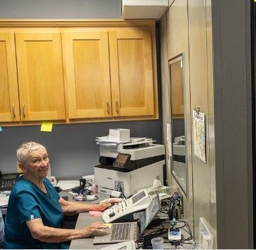 A woman is sitting at a desk with a laptop and a printer.