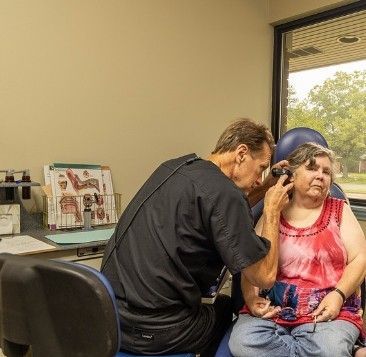 A man is examining a woman 's ear in a chair.