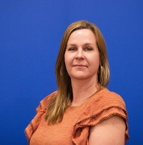 A woman in an orange shirt is standing in front of a blue background.