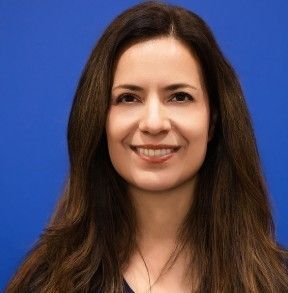 A woman with long brown hair is smiling in front of a blue background.