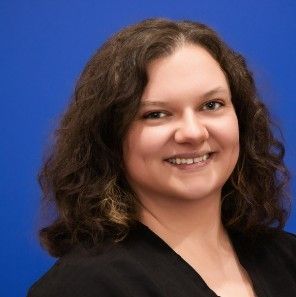 A woman with curly hair is smiling in front of a blue background.