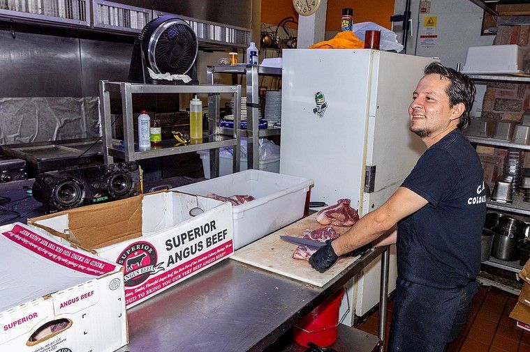 A man is cutting a piece of meat in a kitchen.