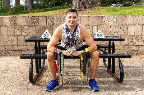 A man is sitting on a picnic table with medals around his neck.