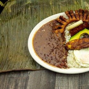 A plate of food with beans , rice , and eggs on a banana leaf.