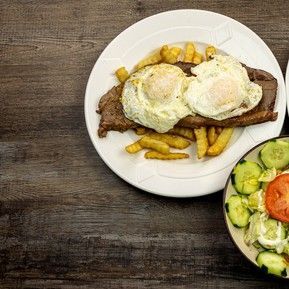 A plate of food with eggs , french fries and a salad on a wooden table.