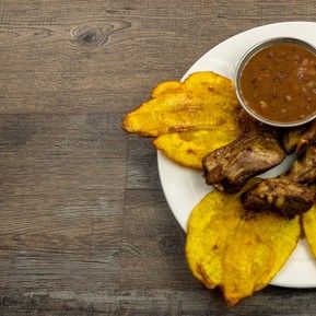 A plate of food with sauce and plantains on a wooden table.