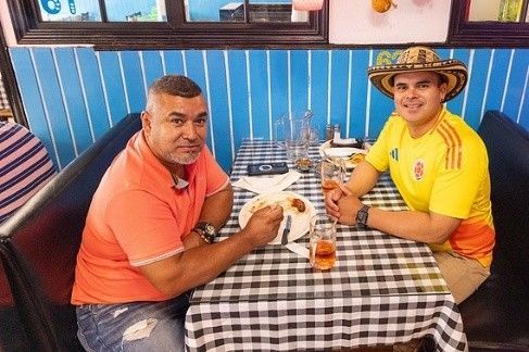 Two men are sitting at a table in a restaurant eating food.