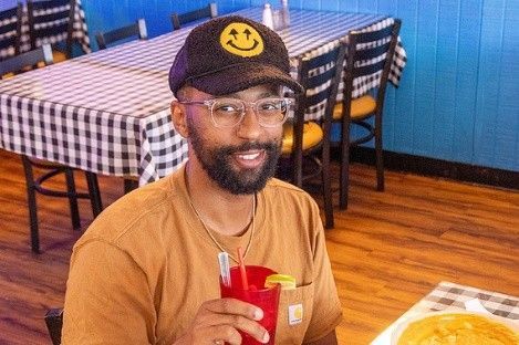 A man is sitting at a table in a restaurant holding a drink.