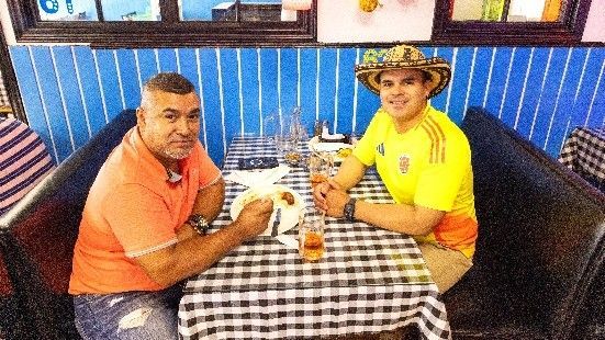 Two men are sitting at a table in a restaurant eating food.