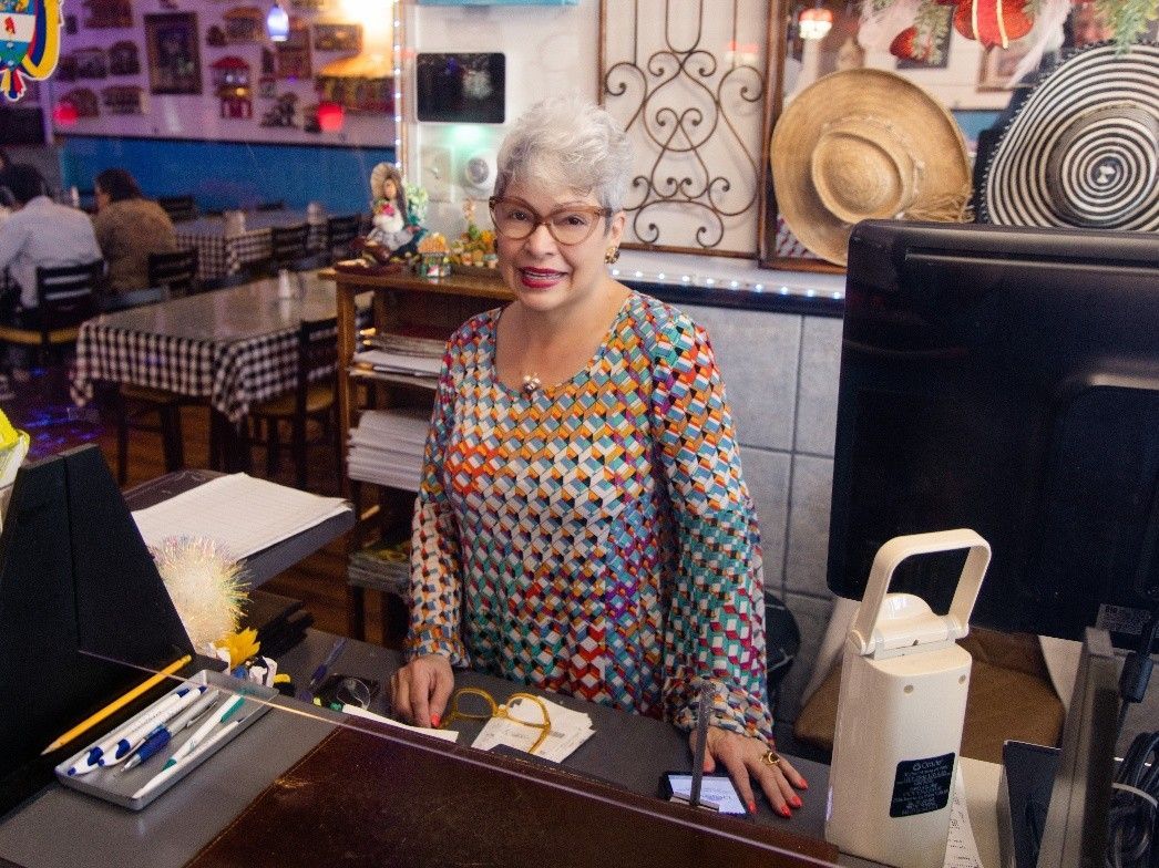 A woman in a colorful shirt is standing behind a counter in a restaurant.
