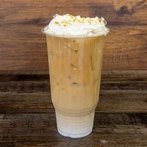 A cup of iced coffee with whipped cream on top is on a wooden table.