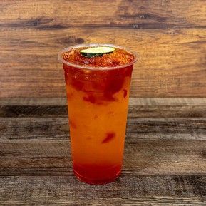 A cup of orange juice with a cucumber on top is sitting on a wooden table.